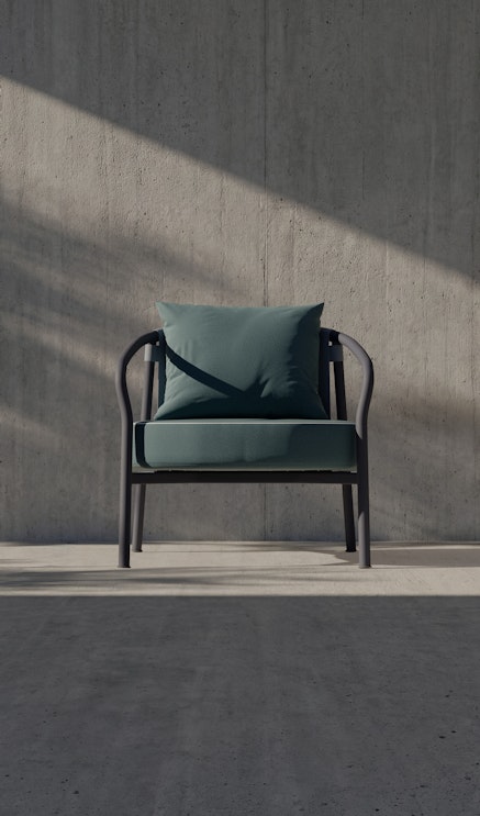 A modern green armchair with a matching cushion sits alone against a textured concrete wall. Sunlight casts diagonal shadows across the minimalist, empty space.