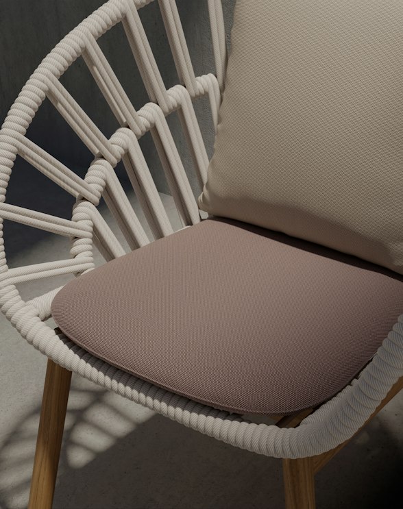 A modern chair with a white woven frame, wooden legs, a light beige cushion on the backrest, and a mauve seat cushion, placed on a sunlit concrete surface.
