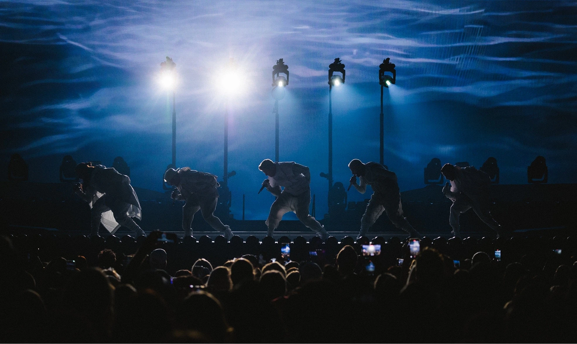 Silhouette of the Backstreet Boys, backlit performing in front of dark blue moody screens content at their Sphere Las Vegas residency.