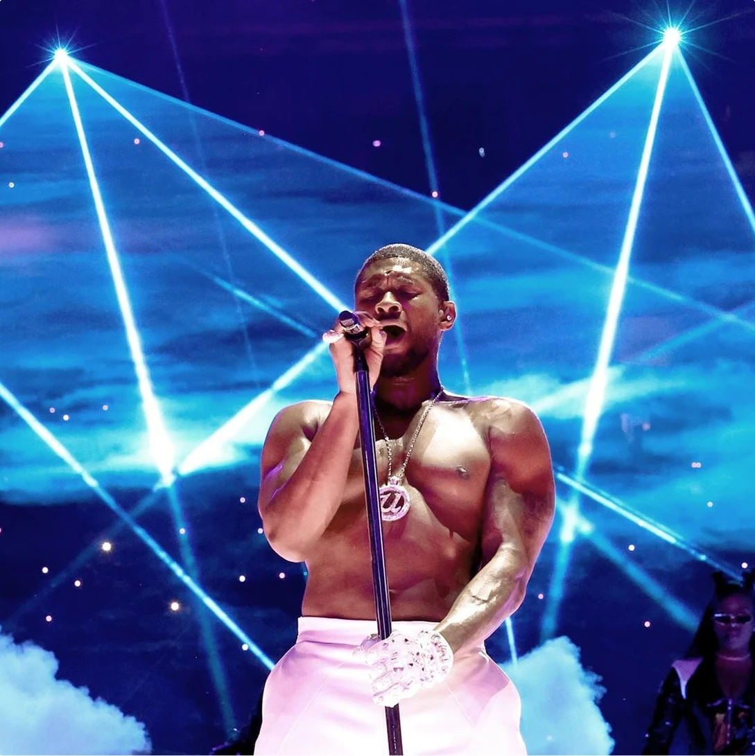 Usher performs at the Super Bowl Halftime Show shirtless with U insignia chain among blue lasers