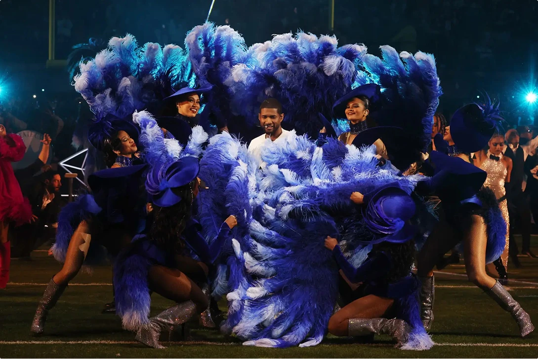 Usher stands among ladies with blue feathered fans on the Super Bowl Halftime Show's field