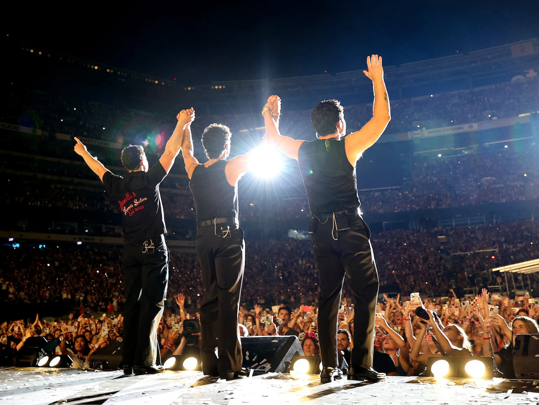 Jonas Brothers - Greetings from Your Hometown Tour - Silent House Jonas Brothers stand on stage holding hands arms up in the air facing the crowd