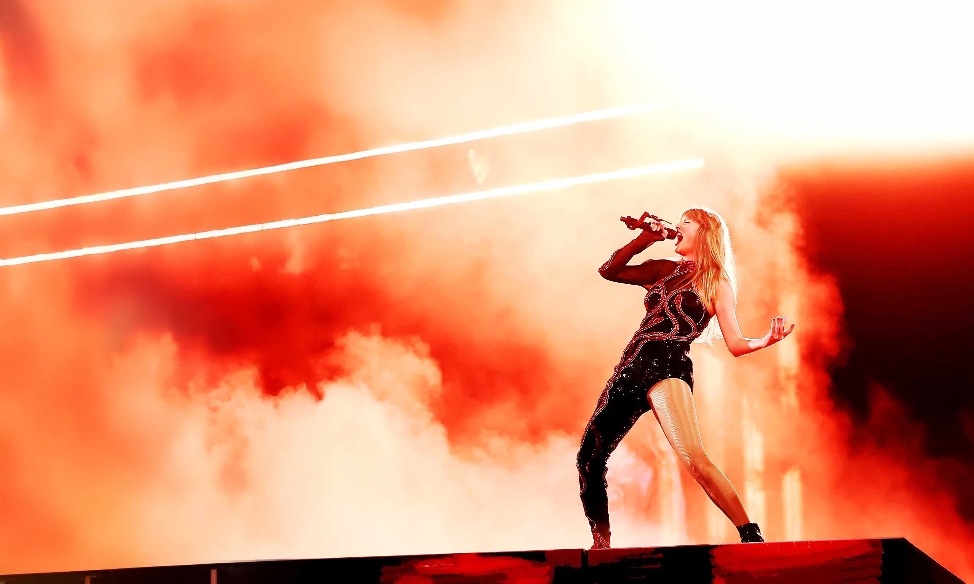 Taylor Swift sings into microphone in a strong pose staged with fog and amber light