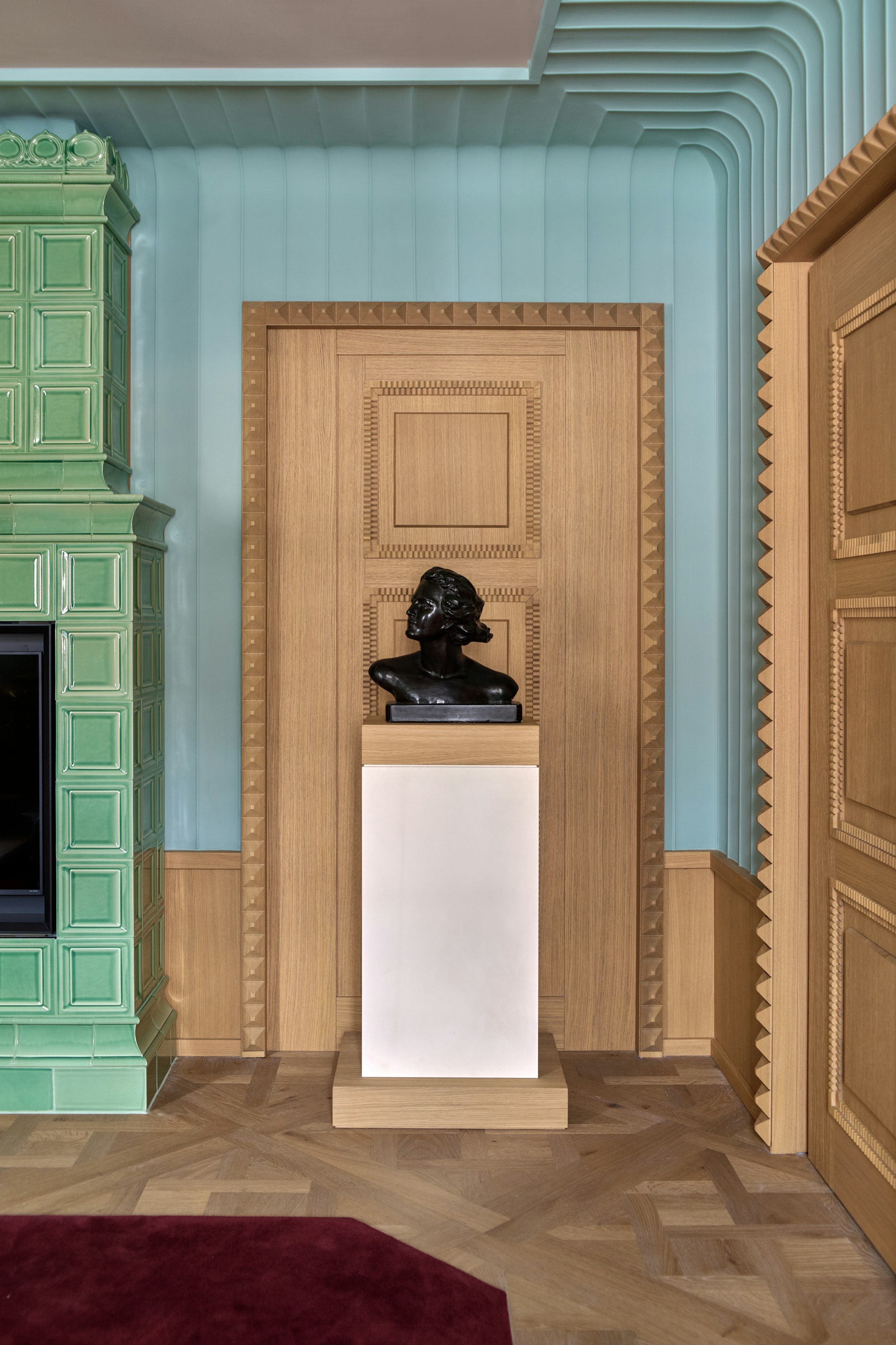 Carved oak door against a pale blue wall, with a bronze bust on a plinth