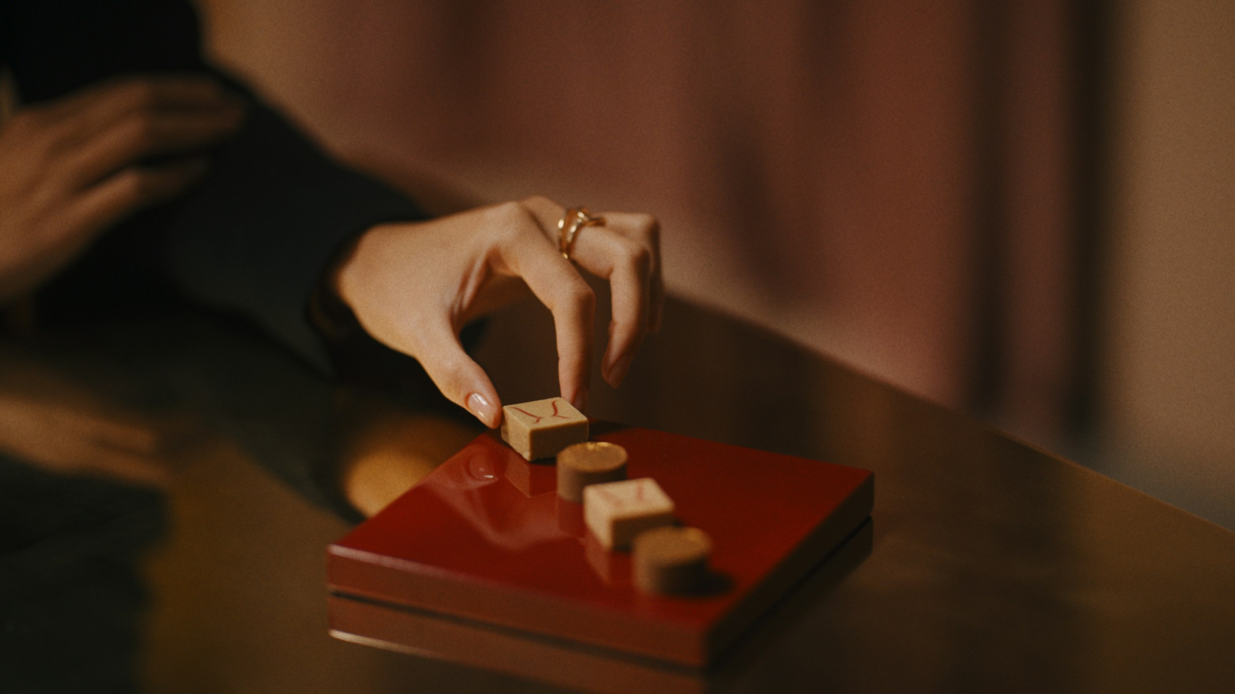 A hand arranging pieces on a red lacquered tray
