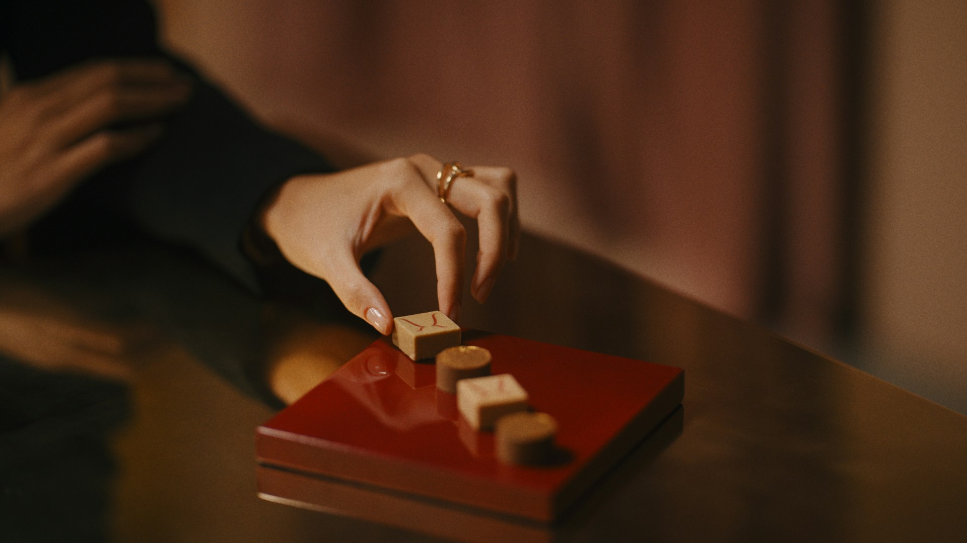 A hand arranging pieces on a red lacquered tray
