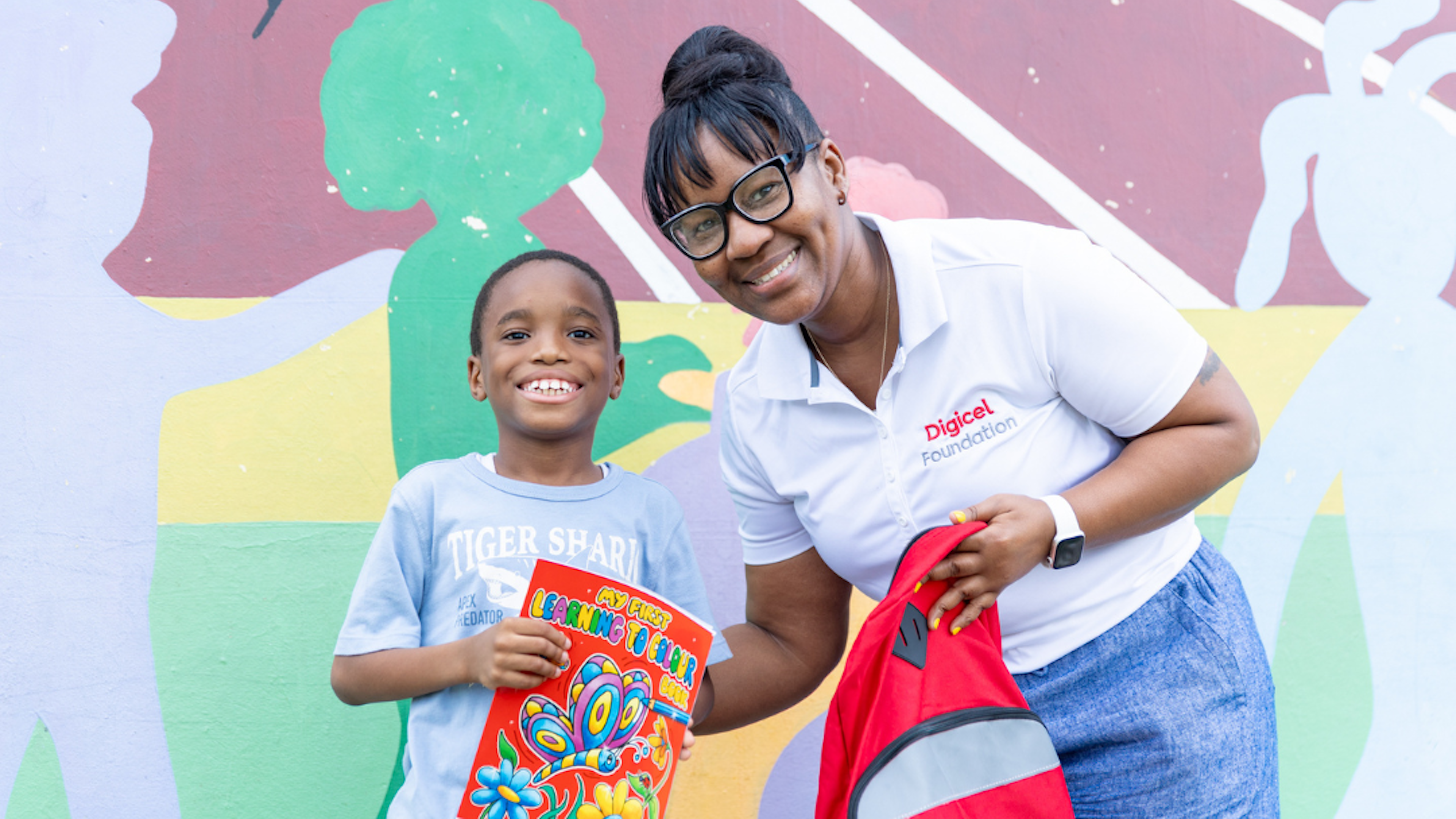 Child holding colouring book next to employee holding backpack