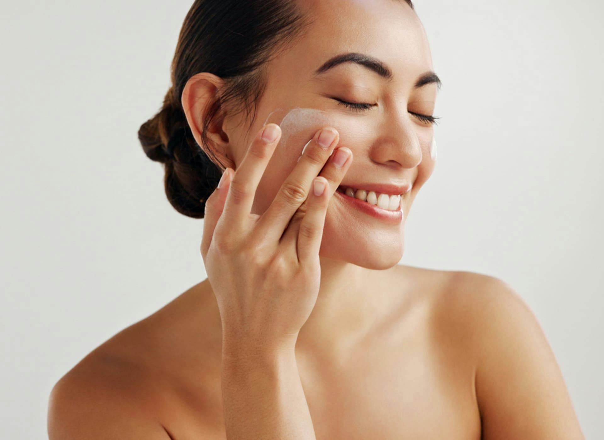 woman smiling and rubbing product on her cheek