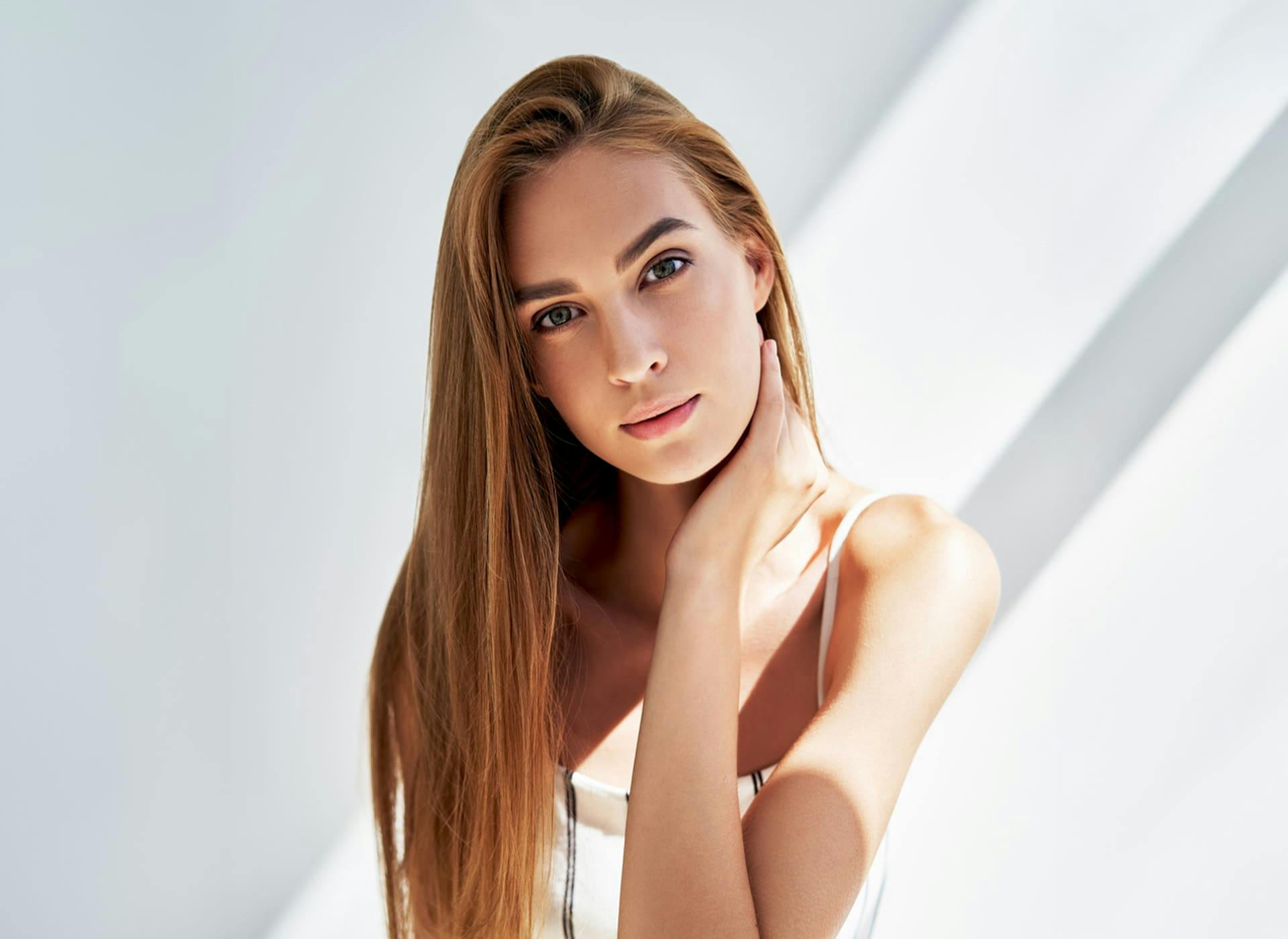 woman with long straight hair while touching her neck with her hand