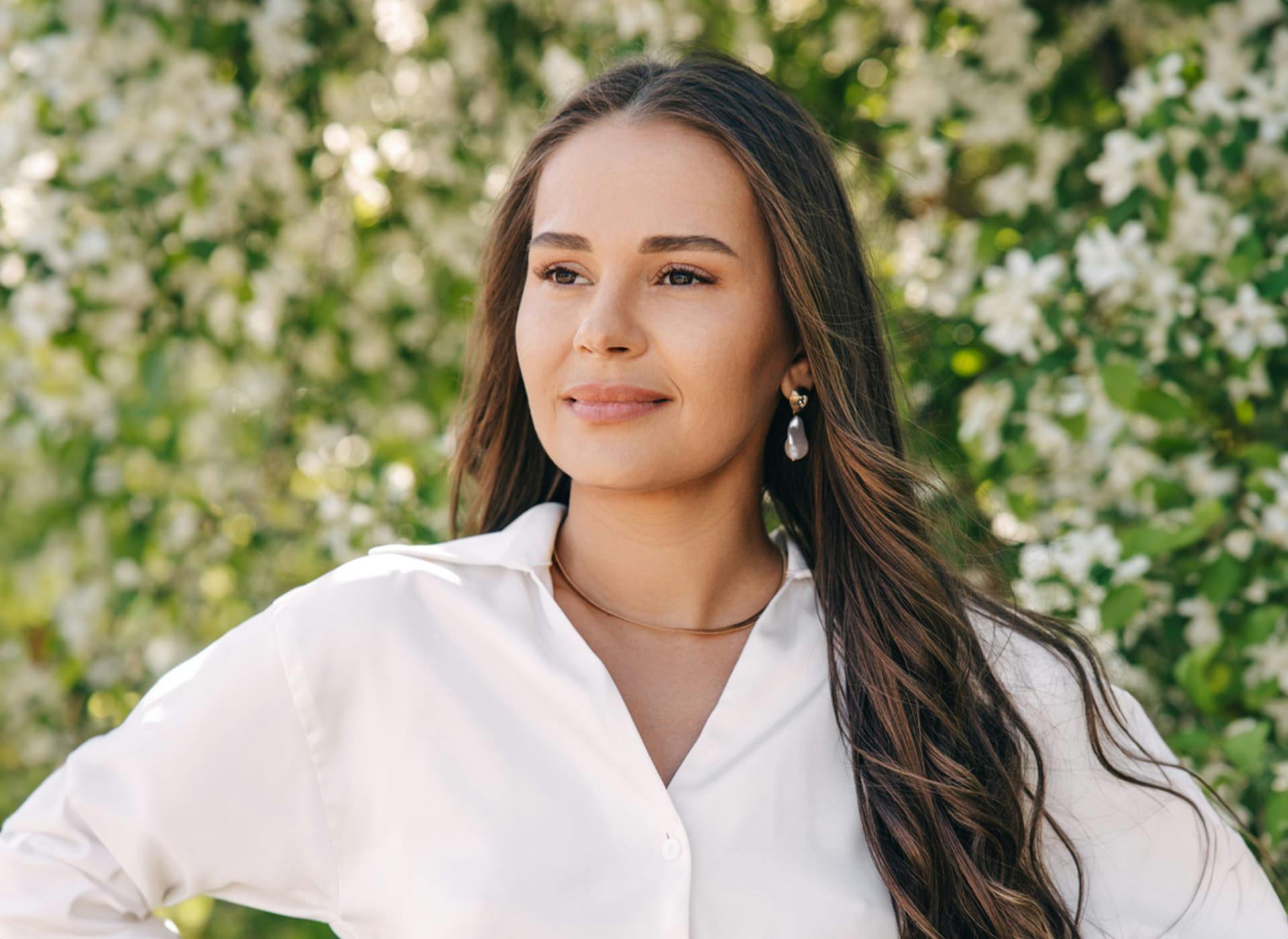 woman standing outside in front of a bush full of white flowers