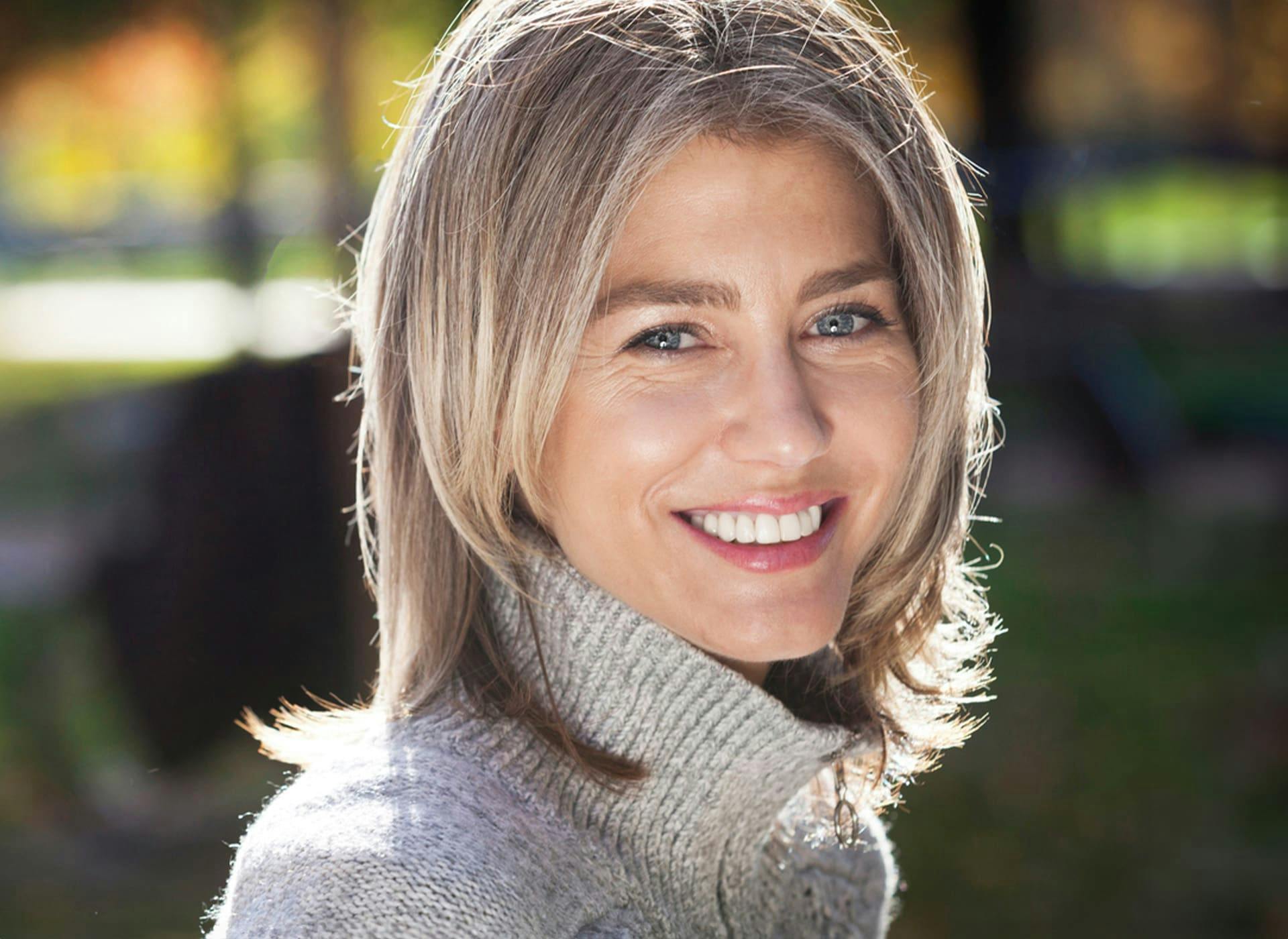 woman with blonde bob smiling in grey turtleneck