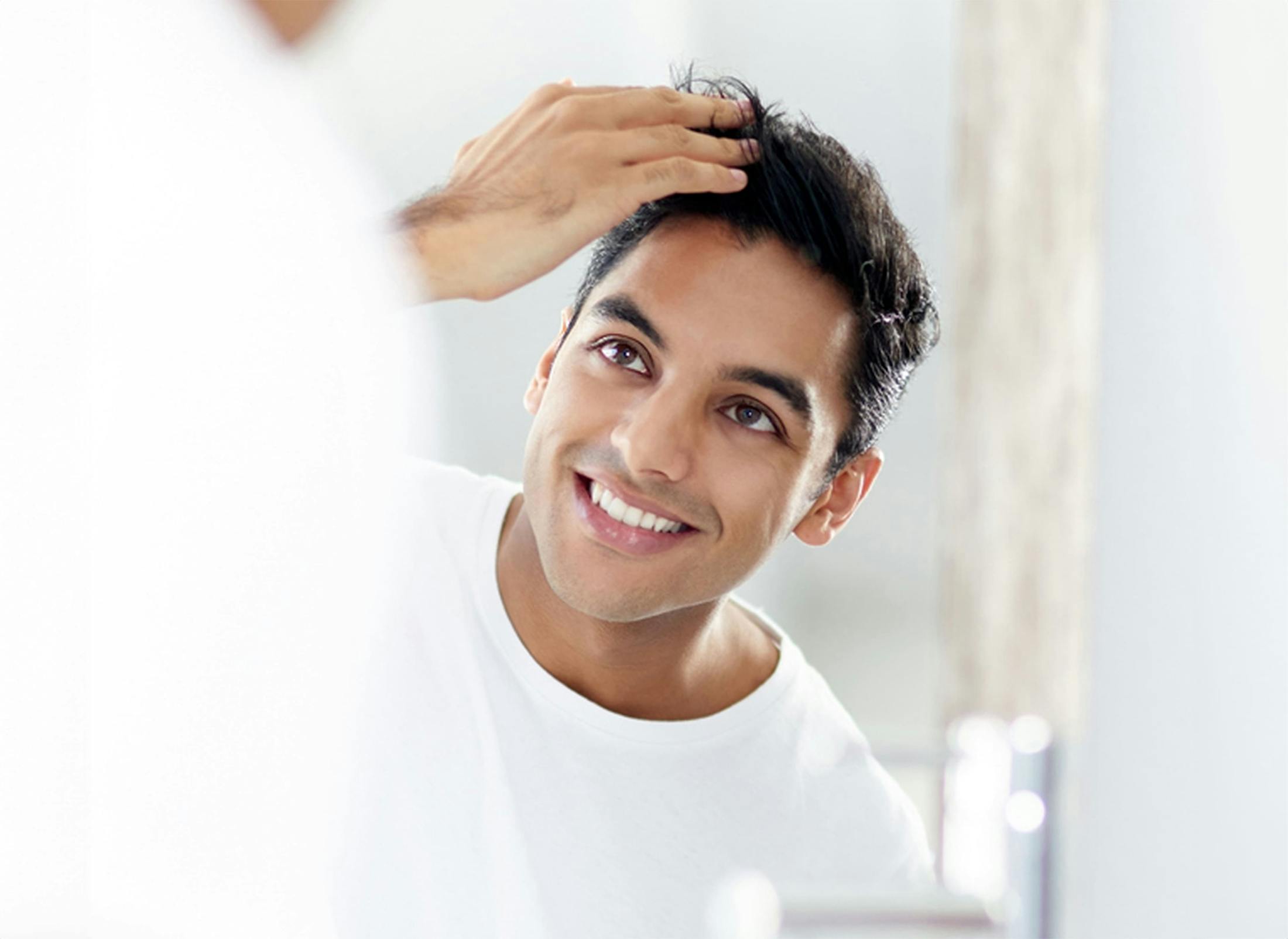 man looking in mirror and fixing his hair