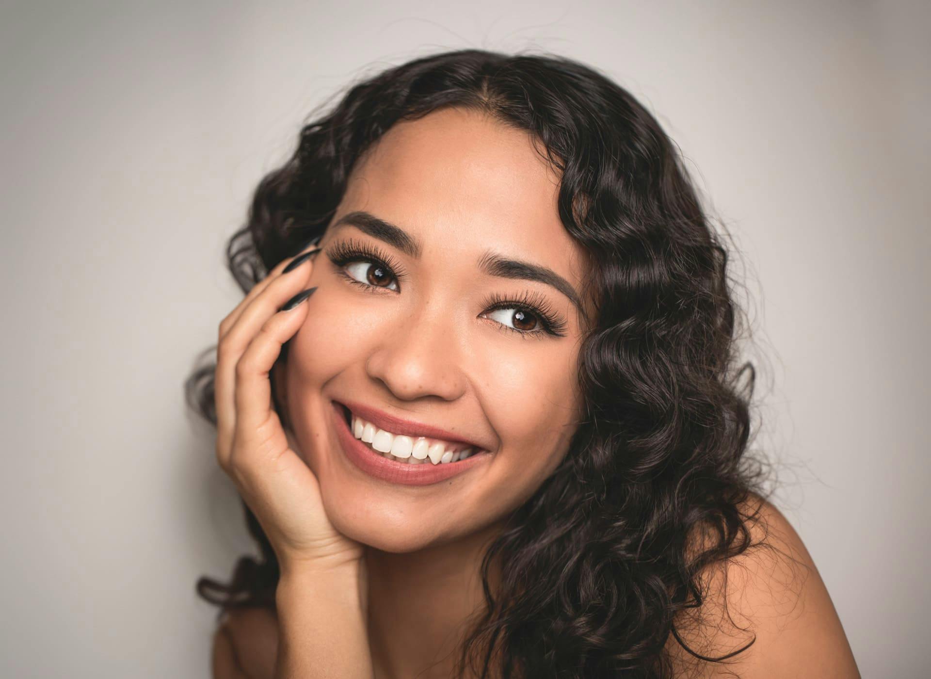woman with curly hair smiling with her hand on her cheek
