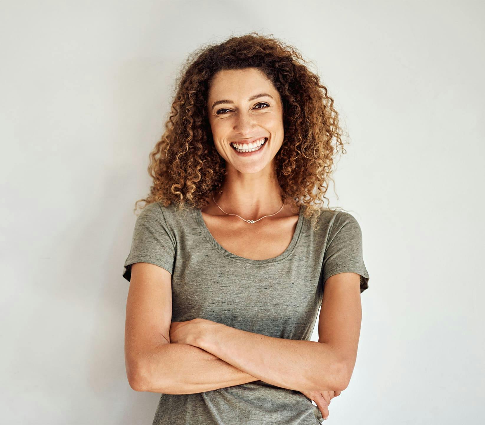 woman with curly hair smiling with her arms crossed