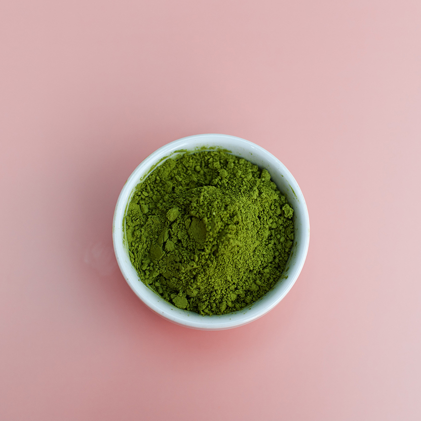 Matcha green tea powder in bowl against pink background.
