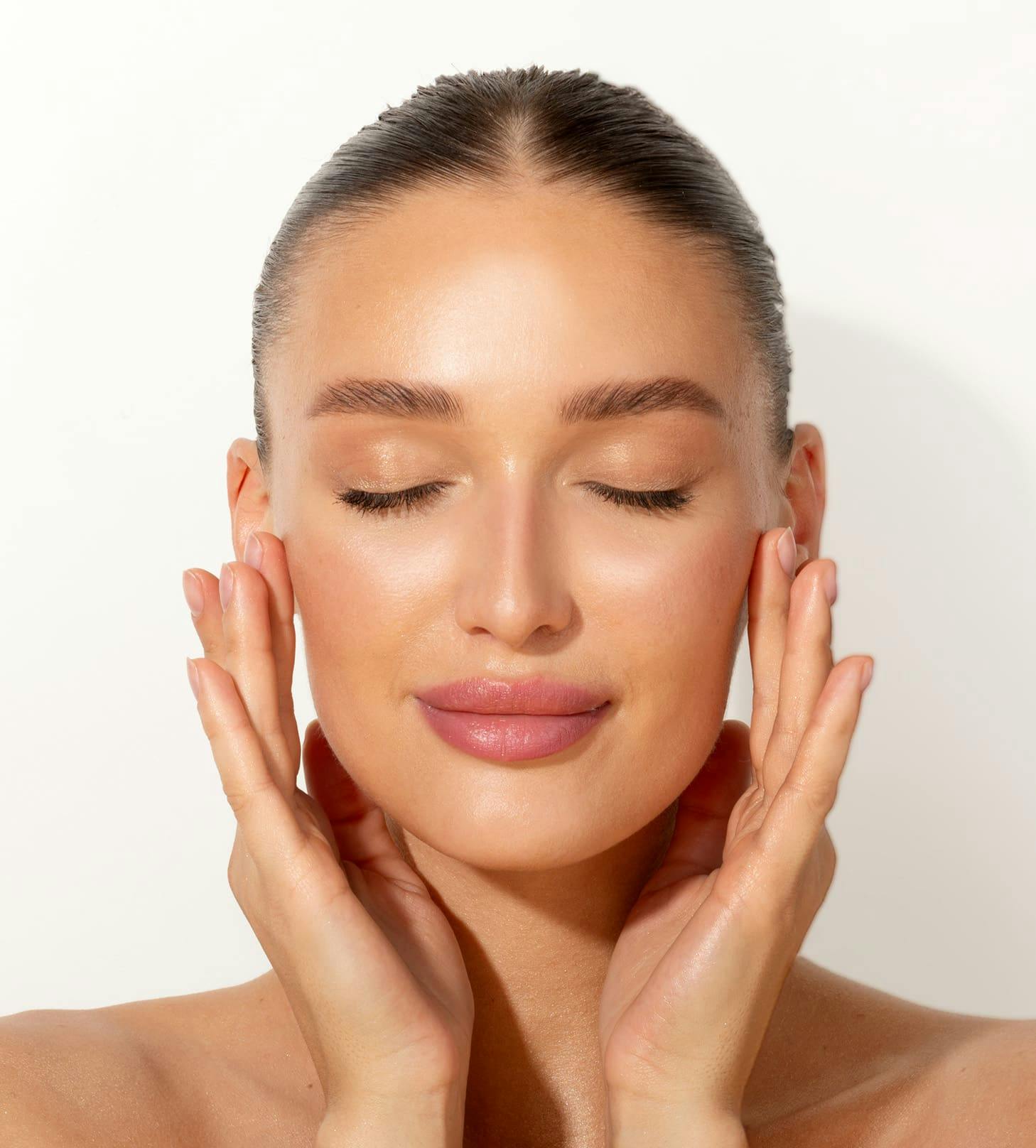 woman with hair tied back and her hands on either side of her face