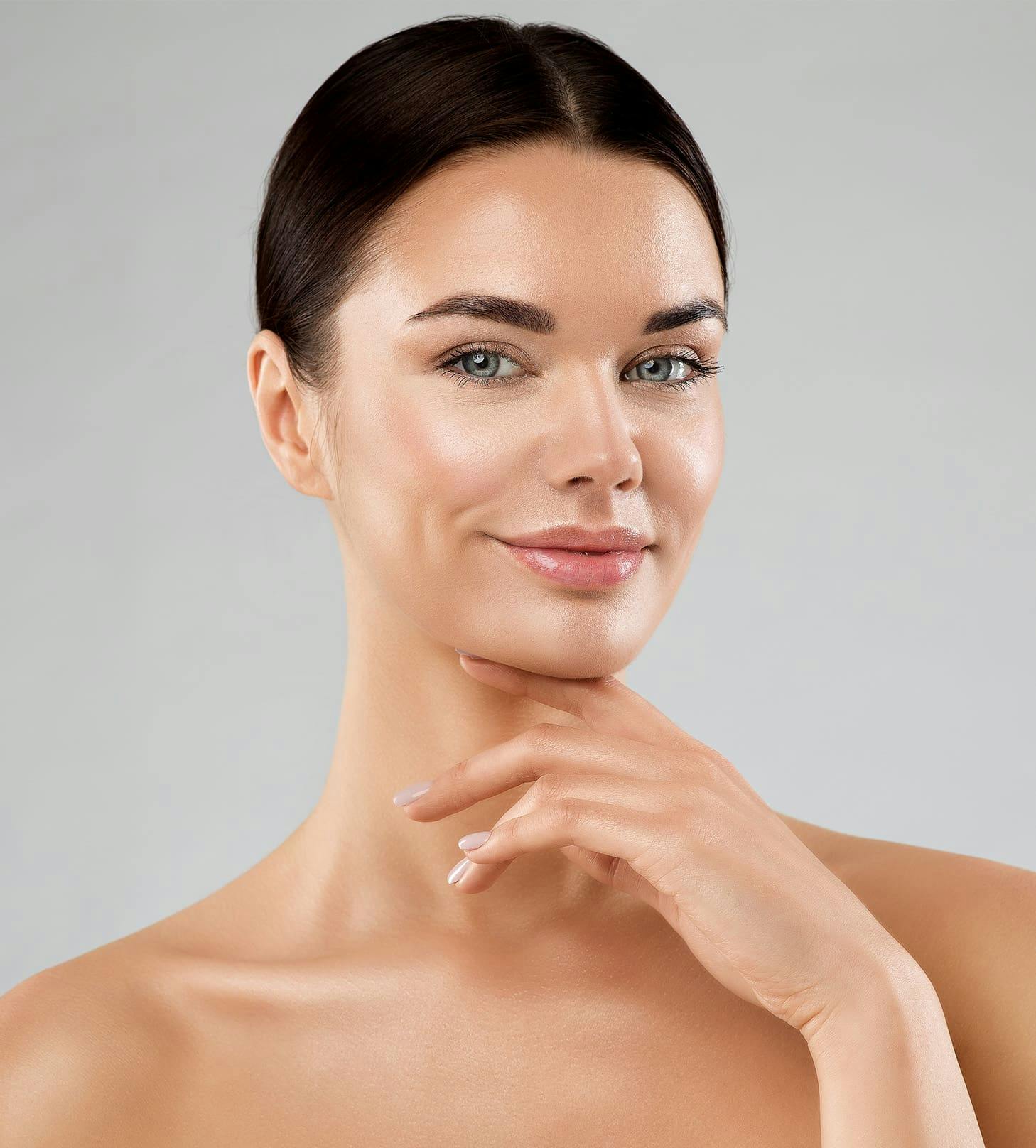 woman with hair tied back smiling with her hand under her chin