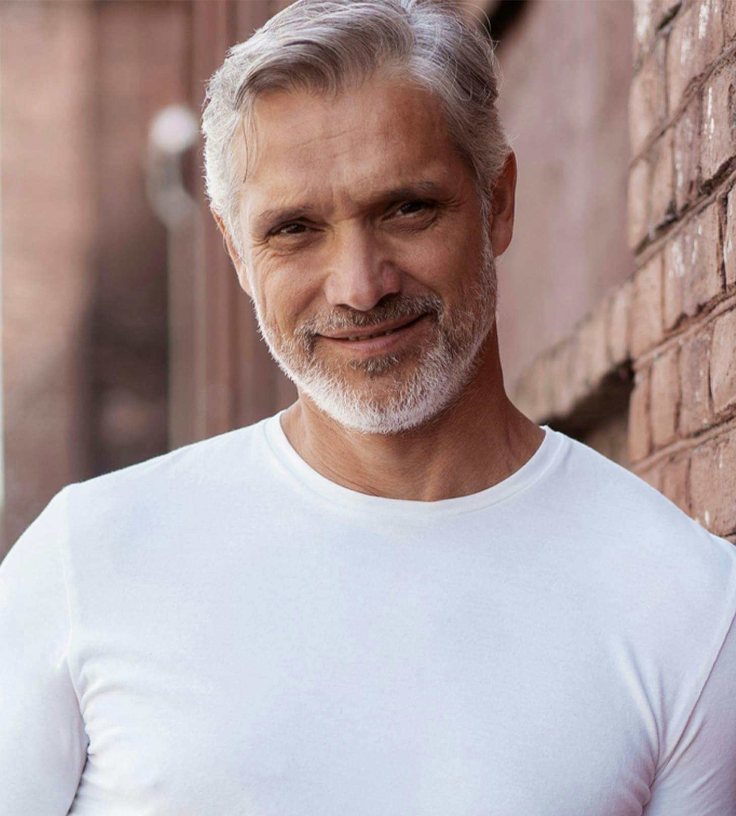 man in white shirt leaning against brick wall smiling
