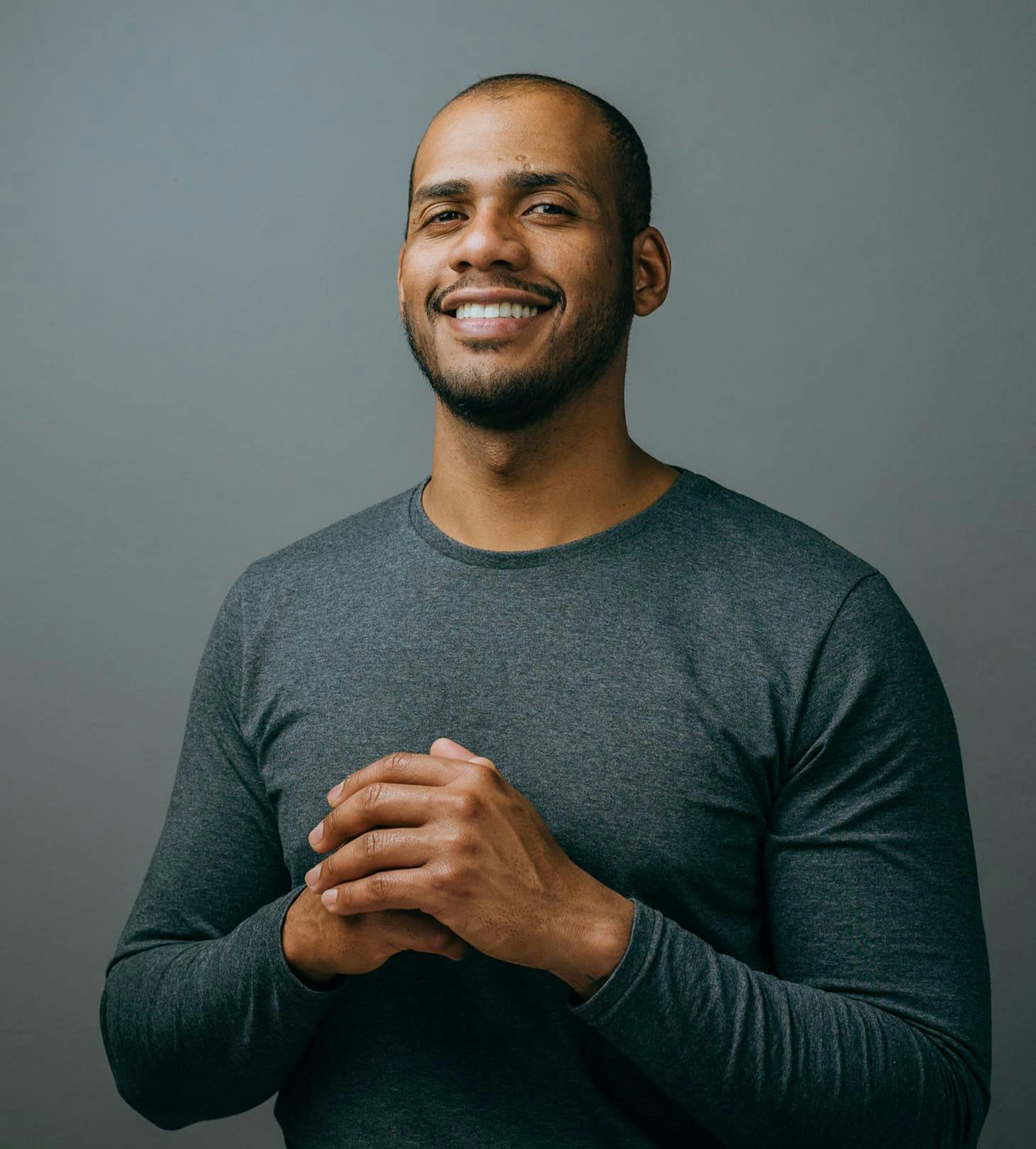 man smiling with his hands together in dark grey long-sleeve
