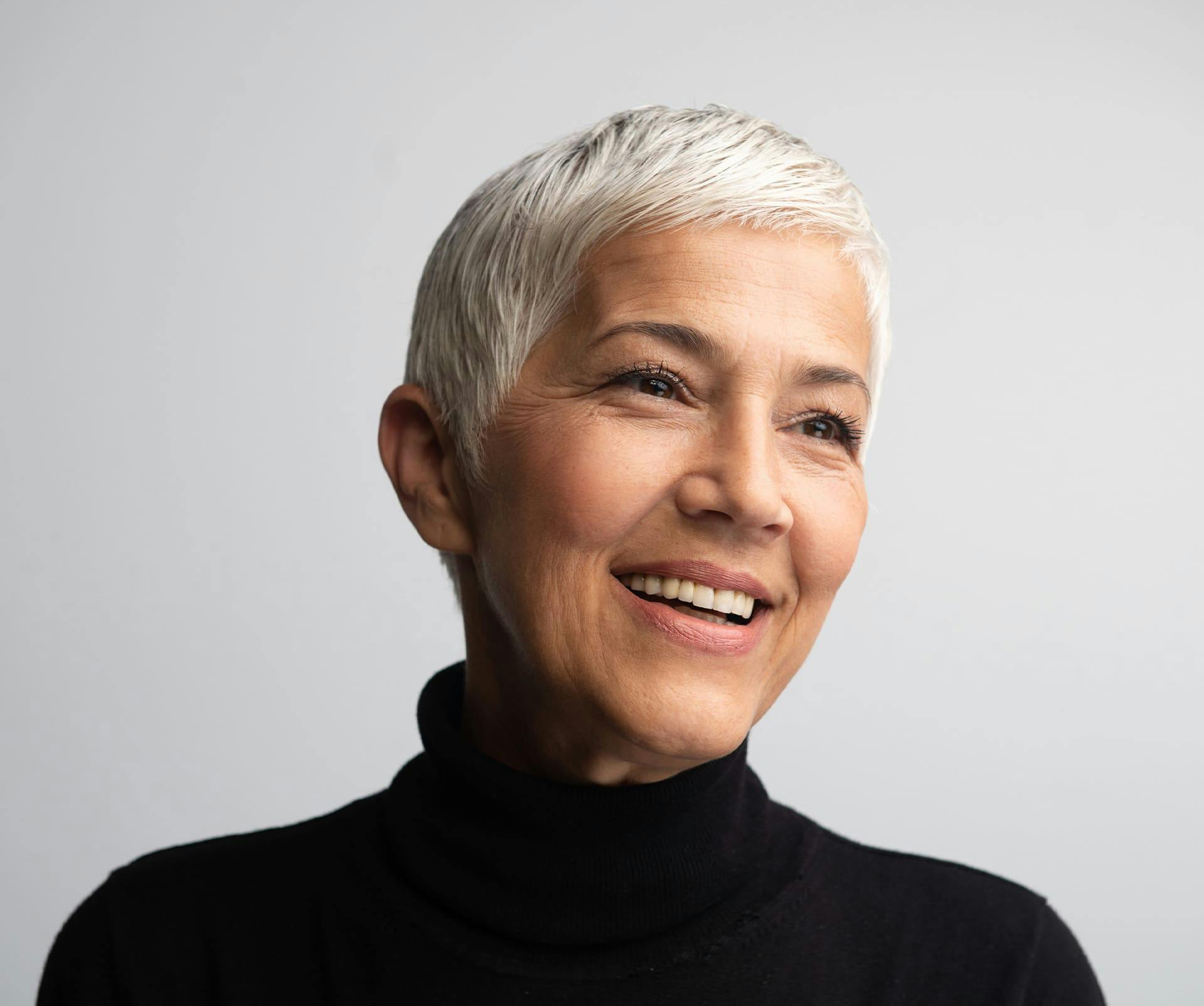 woman with short white hair smiling in black turtleneck