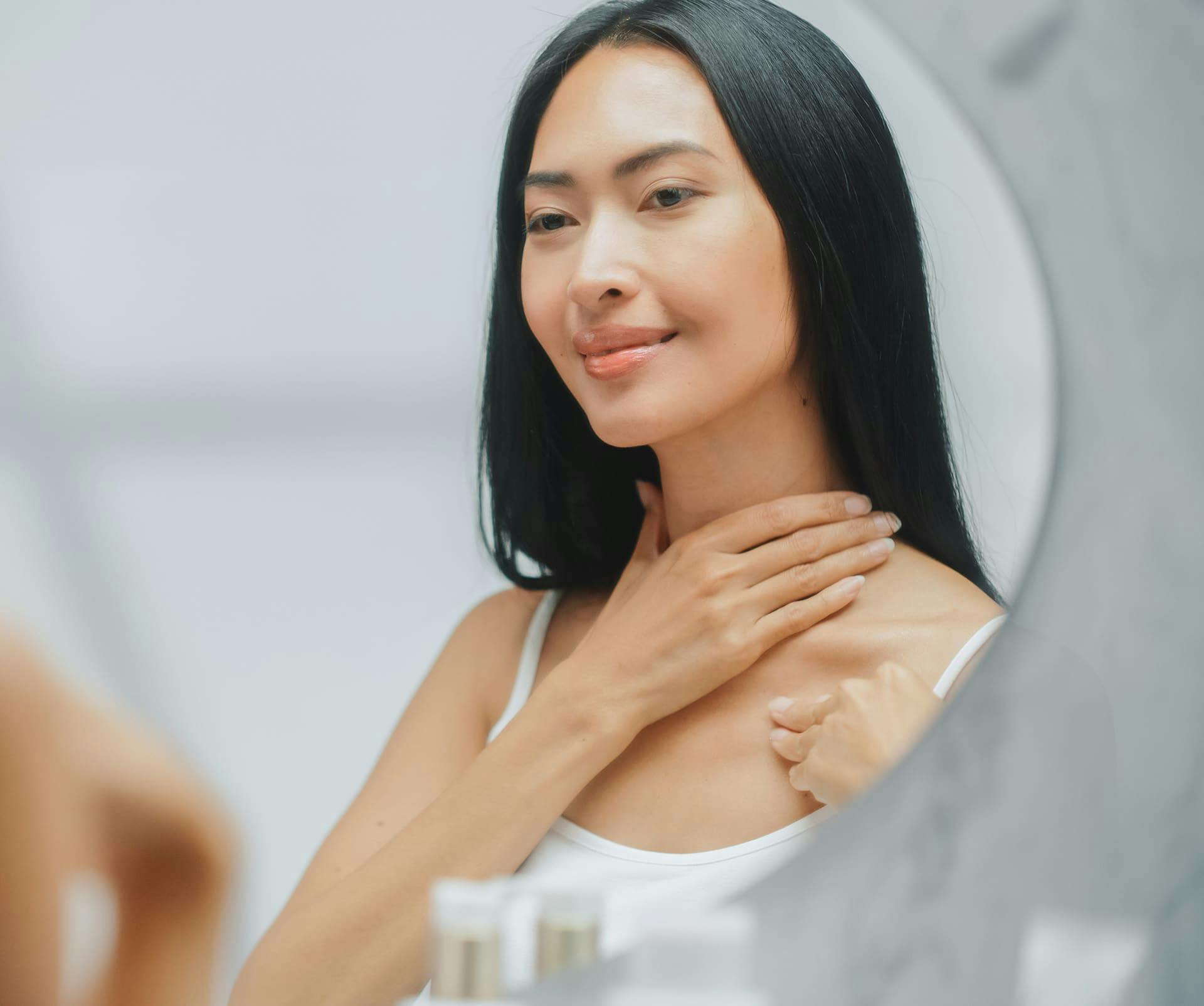 woman smiling in mirror with her hand near her neck
