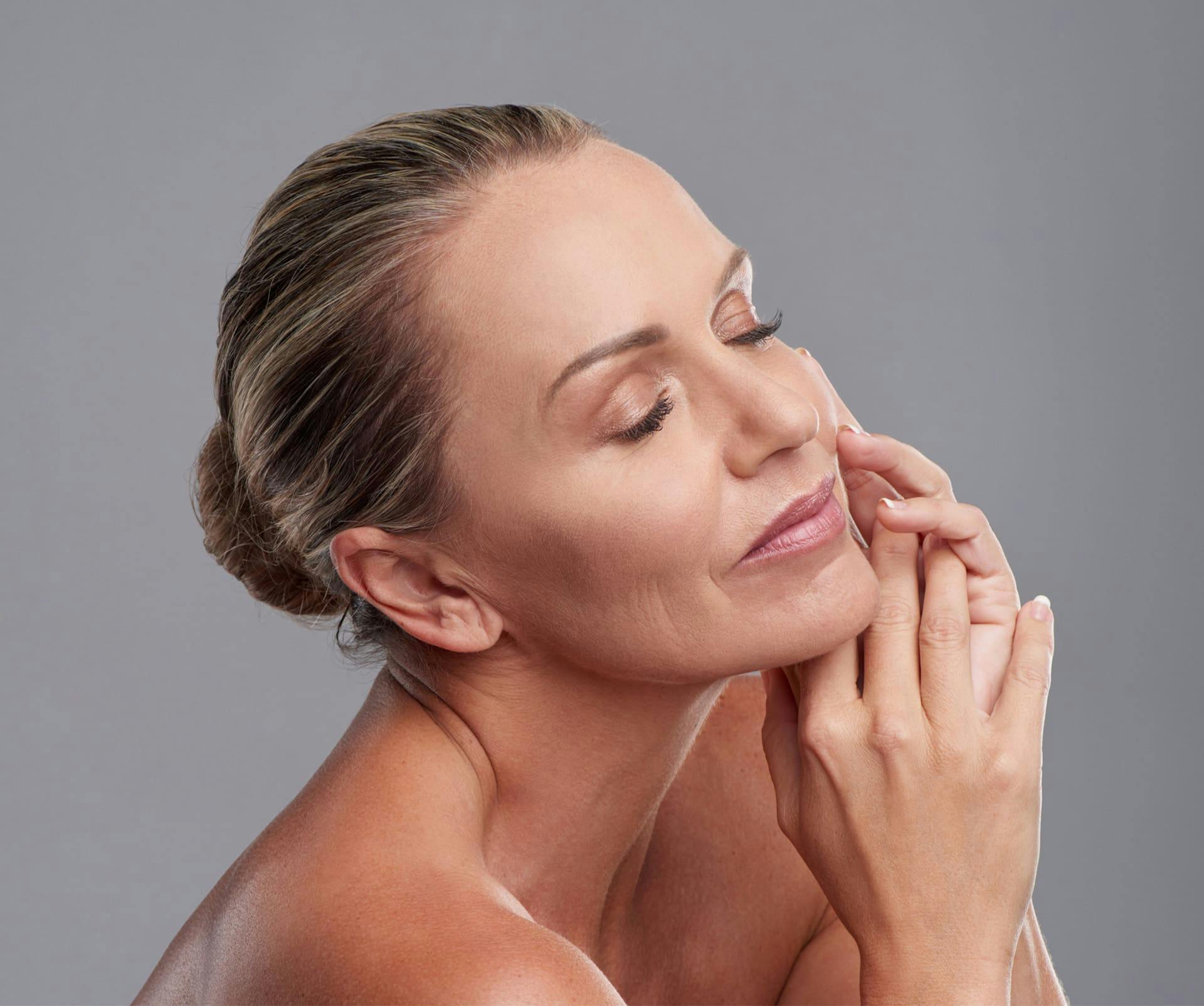 woman with her hands next to her cheek with her hair in a bun