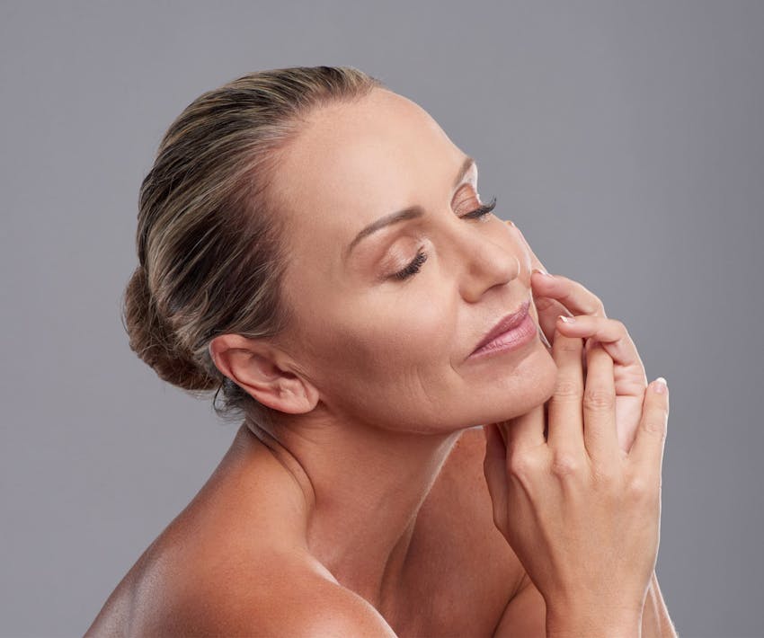 woman with her hands next to her cheek with her hair in a bun