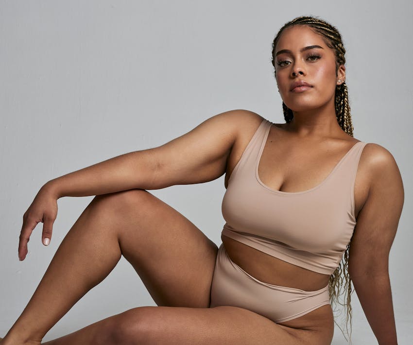 woman sitting with her elbow on her knee in beige underwear set