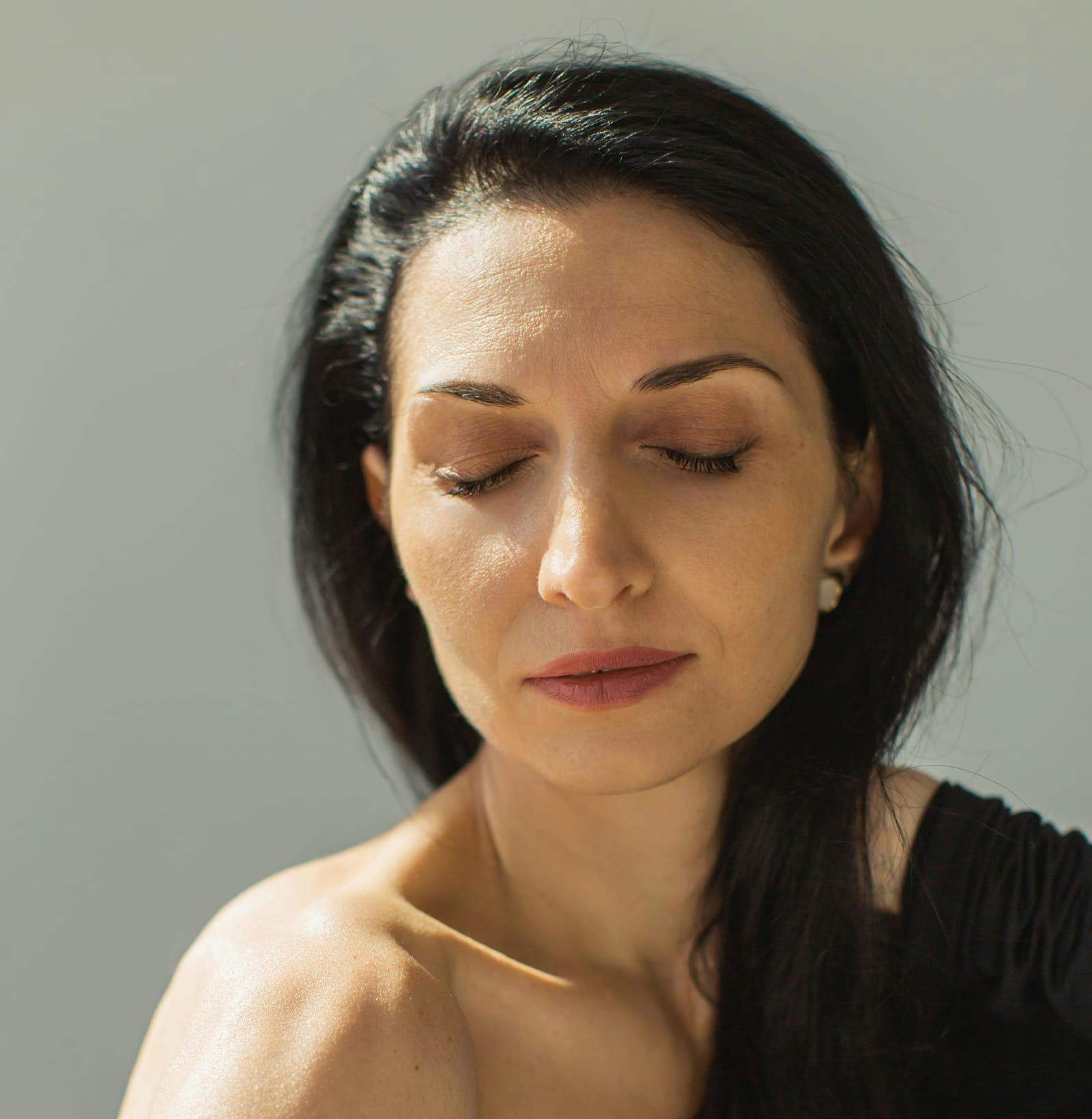 woman in black shirt and hair tucked back with her eyes closed