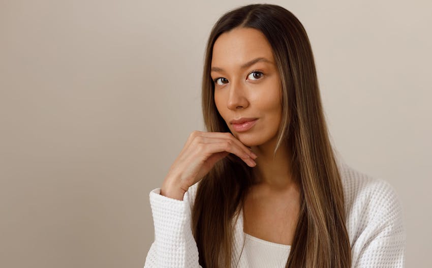 woman in white shirt with white jacket resting hand on jaw