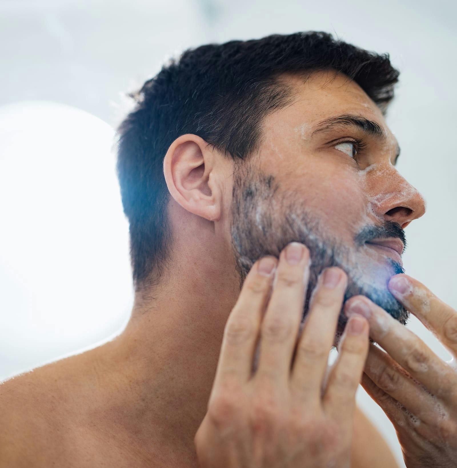 dark haired man washing his face and beard