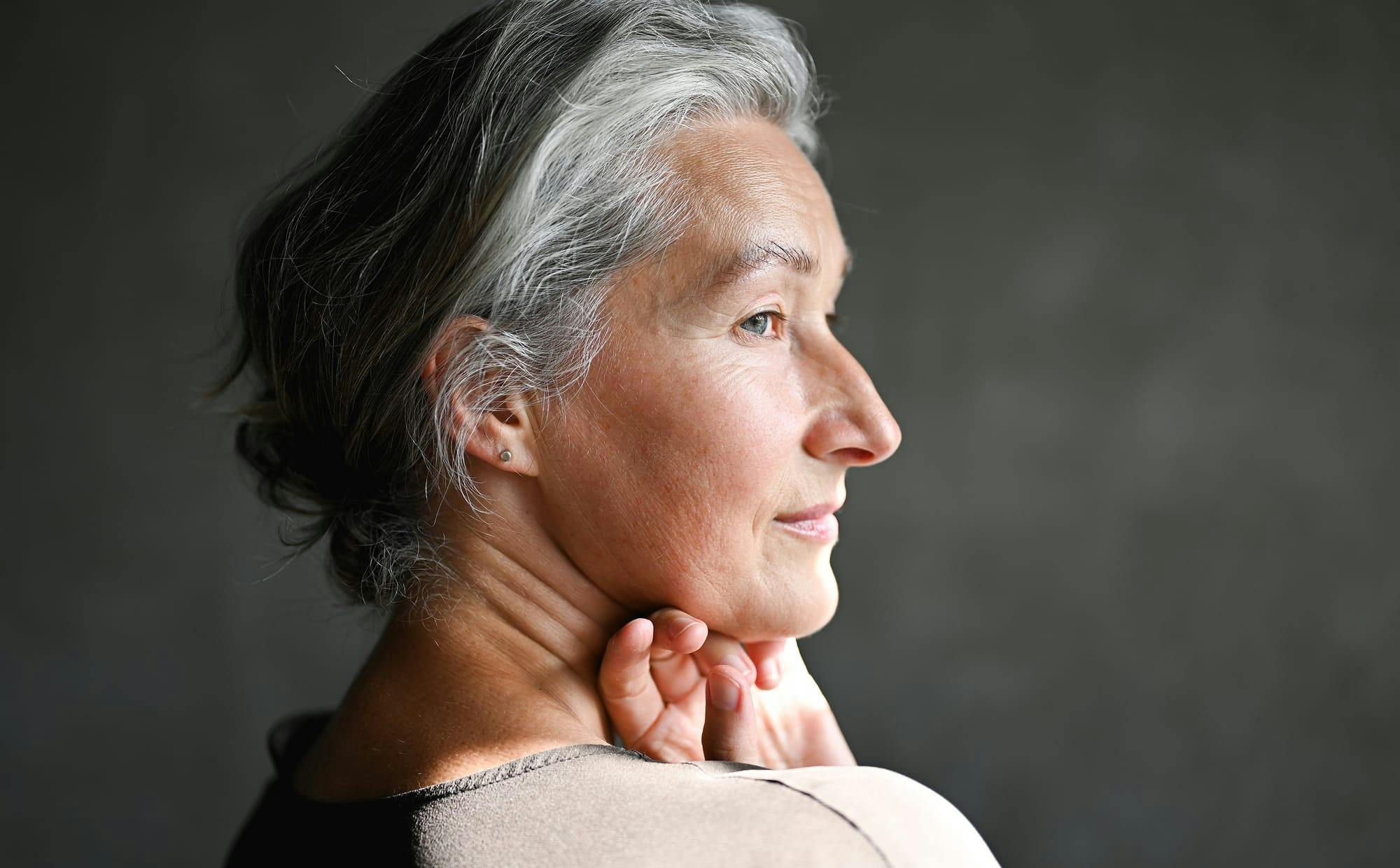 woman in grey shirt looking to the side with hand under chin