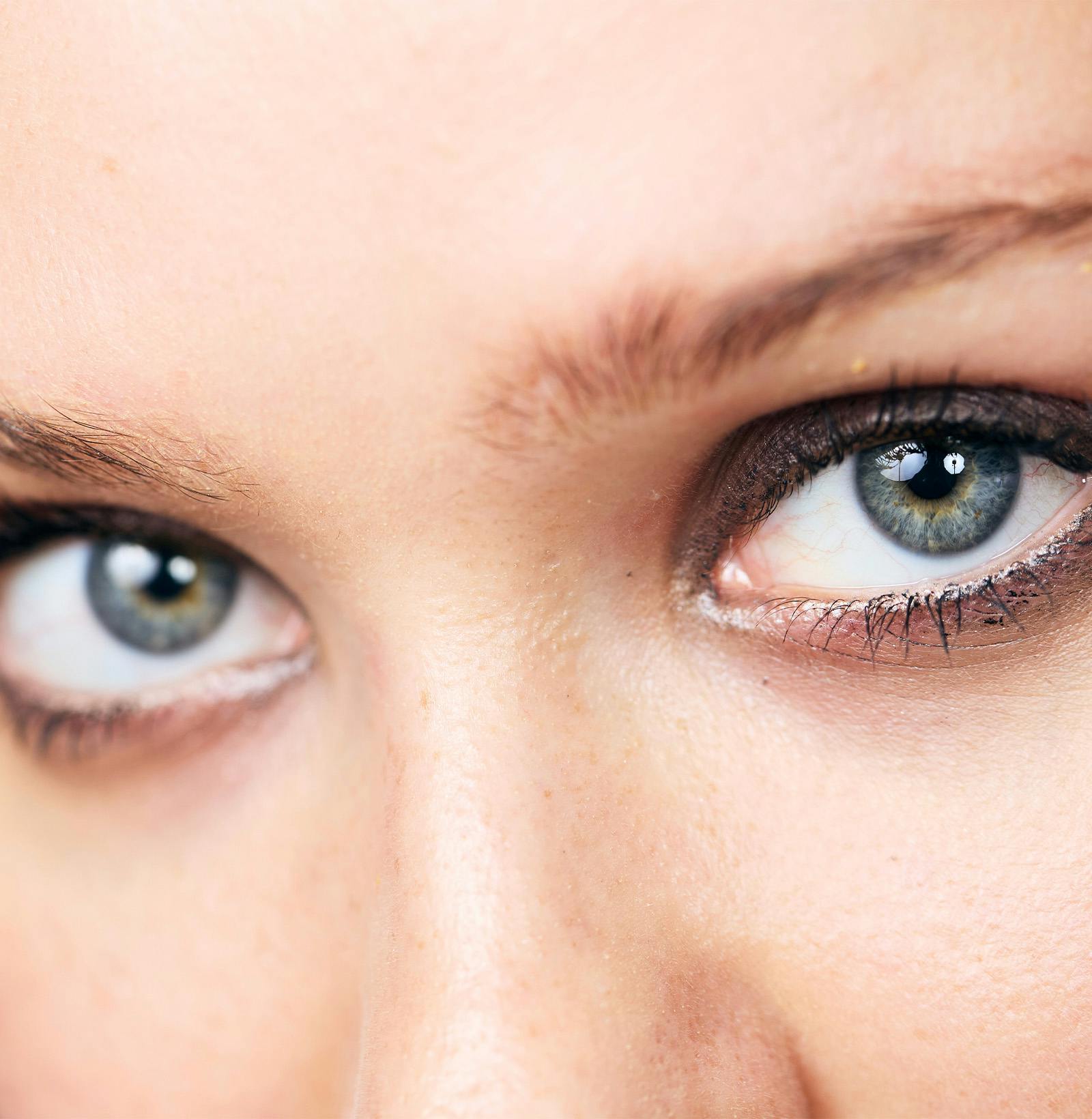 woman looking in mirror while tweezing eyebrows