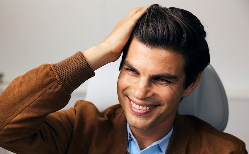 man in patient chair touching side of head smiling