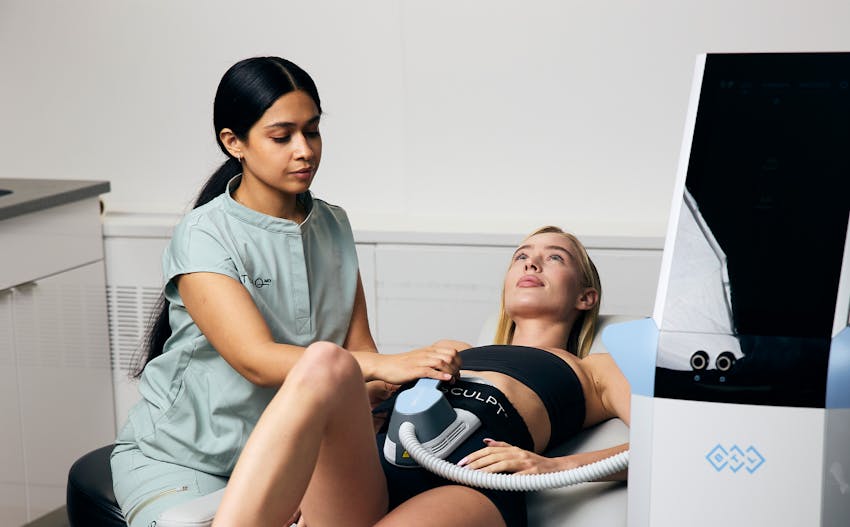 Woman laying on medical bed with Emsculpt equipment attached to her abdomen