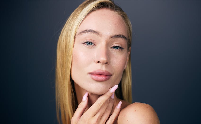blond woman with hair tucked behind one ear and hand resting on chin