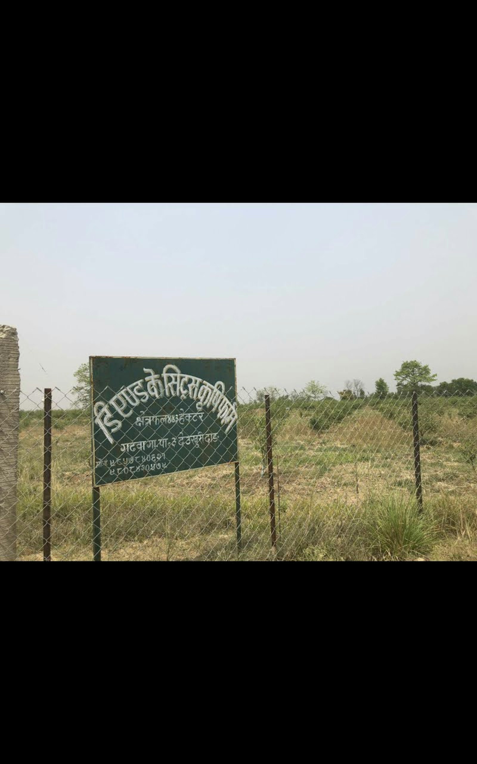 A signboard in Nepali beside a fenced field of grass