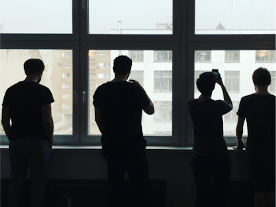 Four people silhouetted against the large office windows, where they are watching and taking photos of snow falling.