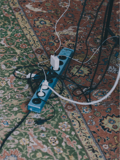 Close-up of an office power strip on a rug, with several laptop chargers and monitor cables plugged into it.