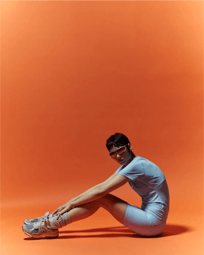 Woman in running gear sitting in front of bright orange background
