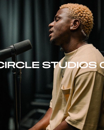 Close up image of artist Godwin singing into a microphone in the White Room at Circle Studios