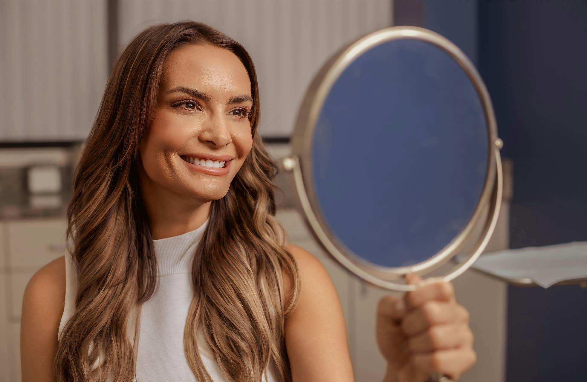 woman smiling into handheld mirror