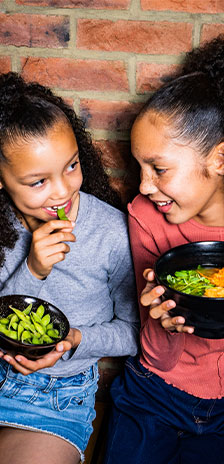 2 girls hold black bowls with edamame and ramen Custom data