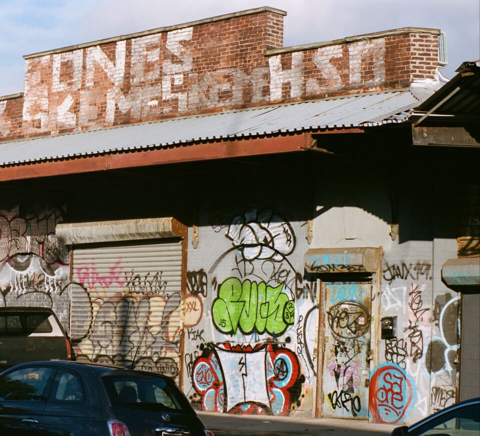 An exterior wall with graffiti and a car in the foreground on a Chicago street. Pirate's creative stuios for musicians, podcasters and dancers coming soon.