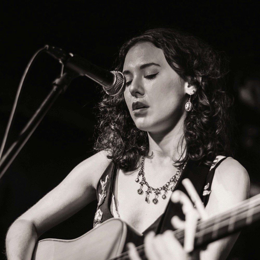 This image may contain: microphone, performer, person, solo performance, guitar, guitarist, music, musician, face, necklace