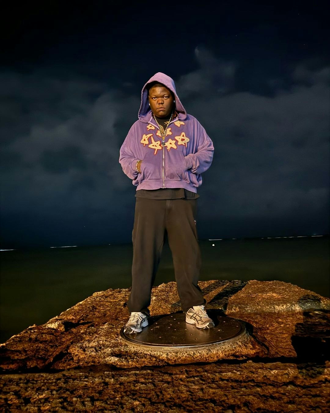 This image may contain: person, standing, clothing, hoodie, sweater, sweatshirt, horizon, sky, rock, sleeve