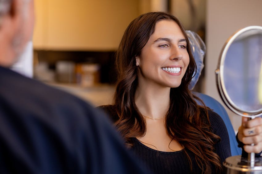woman smiling while looking into handheld mirror