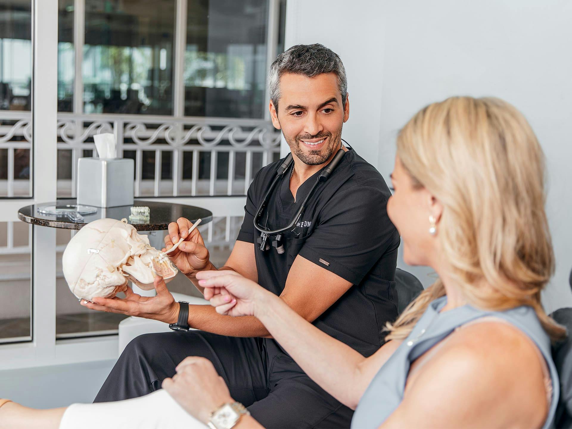 staff member pointing to the teeth on fake skull to patient