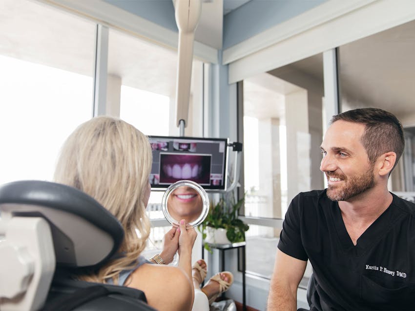 patient looking at teeth in handheld mirror with staff member sitting next to her