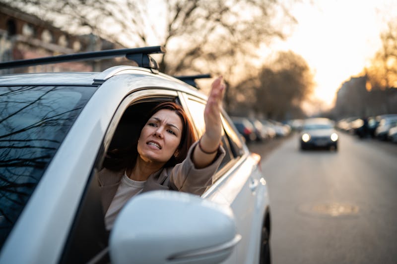woman driving sticking her head and arm out the window in anger
